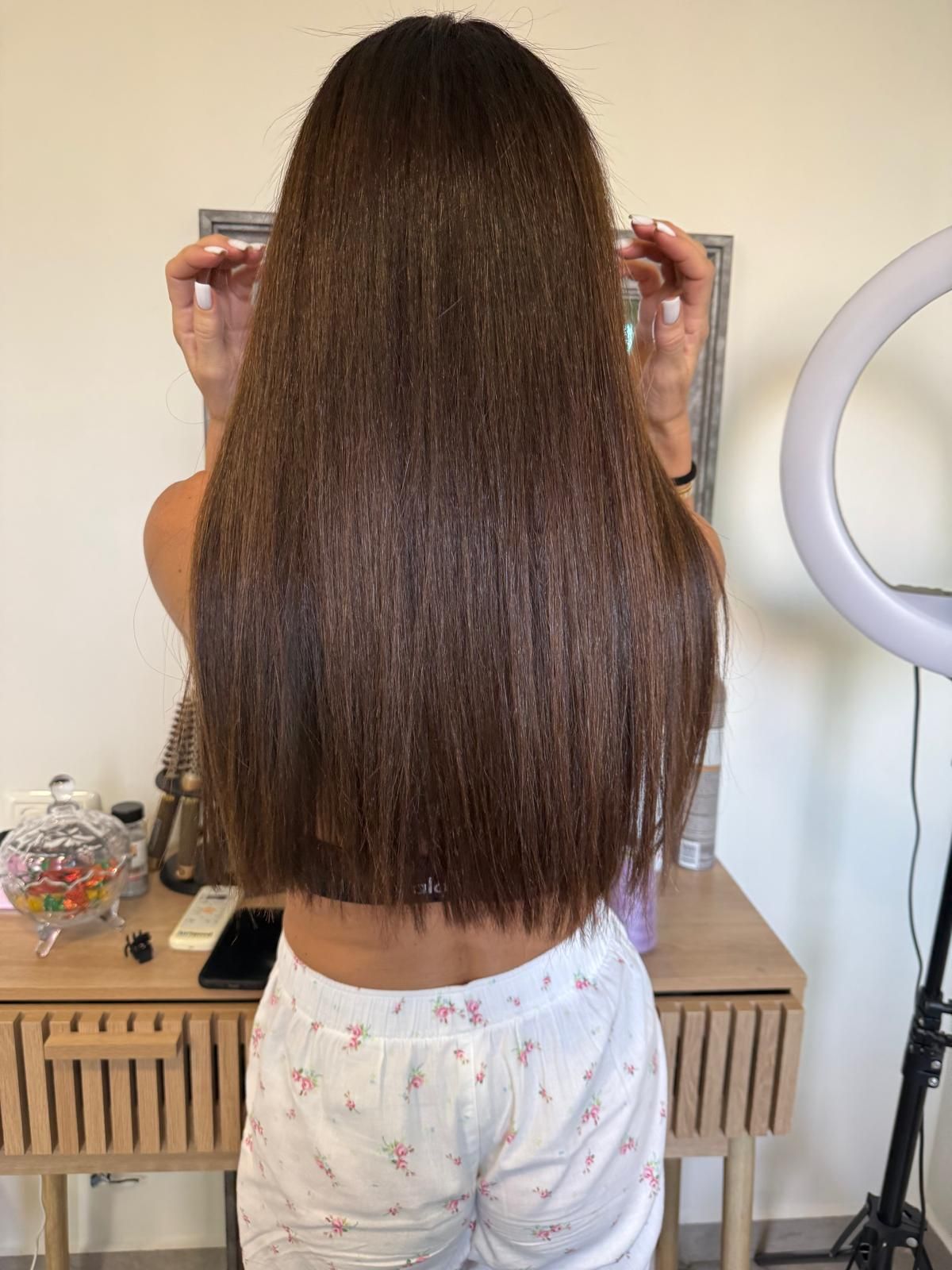 אישה מציגה שיער חום ארוך וישר בעדשה מראה אחורי